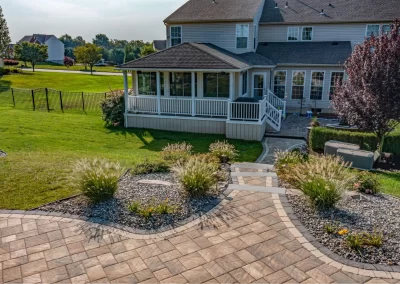 Backyard with a patio, landscaped garden, stone walkway, and a screened porch attached to a house—expertly designed by Solid Brick Contracting, MD, specializing in custom landscaping solutions.