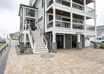 Three-story beach house in Aberdeen, MD, featuring large balconies, white railings, wide stairs, beautiful landscaping, and a spacious paved driveway.