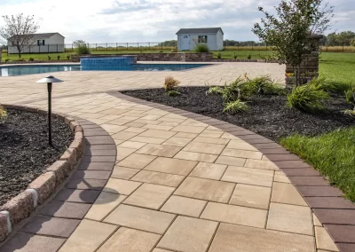 Curved stone walkway by a pool, expertly hardscaping the landscape with mulch, plants, and lawn in Aberdeen, leading toward small sheds—crafted by Solid Brick Contracting.