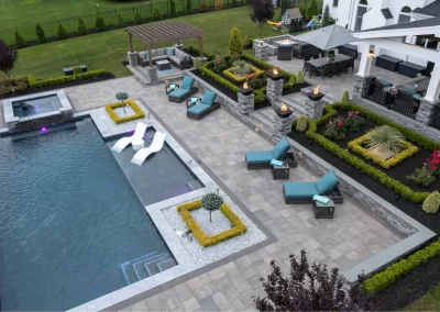 Aerial view of a modern Aberdeen backyard by Solid Brick Contracting, featuring hardscaping, a pool, lounge chairs, fire pits, and landscaped gardens.