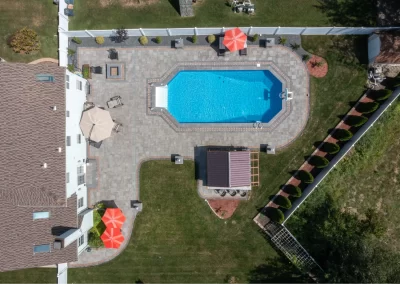 Aerial view of a beautifully landscaped backyard in Aberdeen with a swimming pool, umbrellas, patio area, and lawn, all surrounded by a white fence—quality by Solid Brick Contracting.