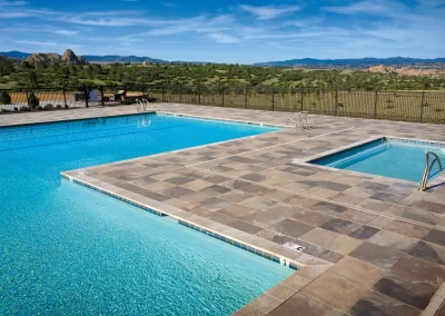 Outdoor swimming pool and hot tub with tile deck, expertly crafted by Solid Brick Contracting, overlooking a scenic landscape of hills and blue sky—perfect for enjoying premium hardscaping and landscaping.