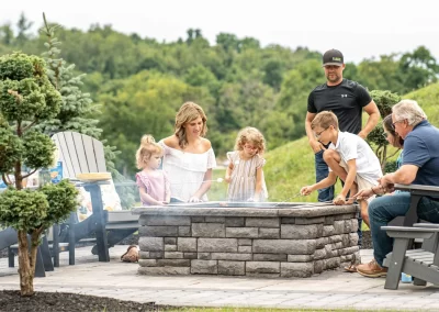 A family gathers around an outdoor fire pit, roasting marshmallows together on a beautifully landscaped patio crafted by Solid Brick Contracting in MD.