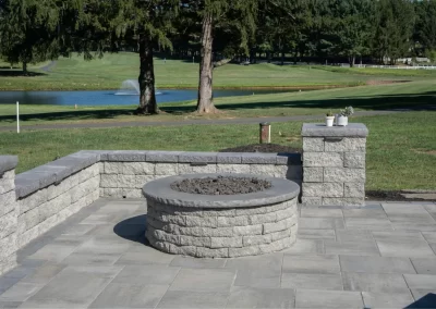 Stone fire pit on a patio with a lake, fountain, and trees in the background—crafted by Solid Brick Contracting for stunning Aberdeen landscaping.