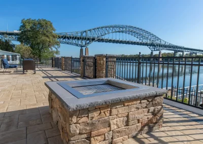 Stone fire pit on a patio featuring expert hardscaping, overlooking a river with Aberdeen’s large arched bridge in the background on a clear day.