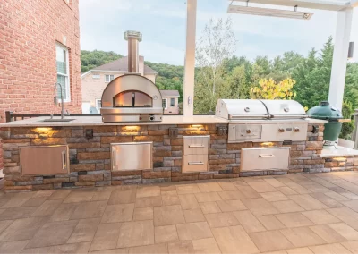 Outdoor kitchen by Solid Brick Contracting features brick and stone counters, wood-fired oven, stainless steel grill, sink, and storage drawers—perfect for MD landscaping projects.