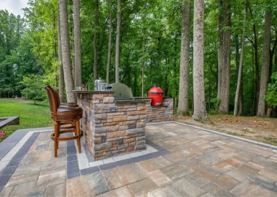 Outdoor patio in Aberdeen, MD, with a stone bar, grill, two chairs, and tall trees—crafted by Solid Brick Contracting.