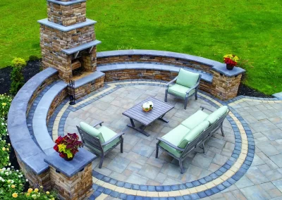 Modern patio with stone fireplace, green lawn, outdoor seating, and potted plants on a paved circular area—expert landscaping by Solid Brick Contracting brings Aberdeen style to your outdoor space.