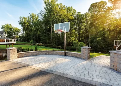 Outdoor basketball hoop on a stone-paved court, expertly hardscaped by Solid Brick Contracting in Aberdeen, with trees and sunlight brightening the scene.