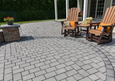 Two wooden chairs and a table with drinks on a gray stone patio showcase elegant hardscaping near an Aberdeen home, with a potted plant adding to the charming landscaping.