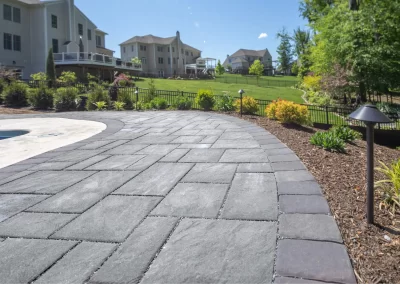 Curved stone patio walkway with landscape lighting, mulch, and plants in a suburban Aberdeen backyard—expertly crafted by Solid Brick Contracting for stunning landscaping appeal.