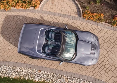 A silver convertible sports car parked on a stone driveway in Aberdeen, viewed from above, with vibrant flowers and expert landscaping on the sides.
