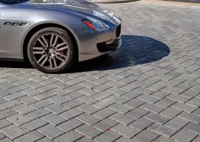 Silver car parked on a driveway with gray stone pavers, crafted by Solid Brick Contracting, in front of a white house with black garage door—a perfect example of quality hardscaping in MD.