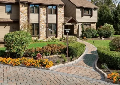 A paved walkway leads to a two-story house with stone accents, garden beds, and manicured bushes, showcasing beautiful landscaping in Aberdeen, MD.