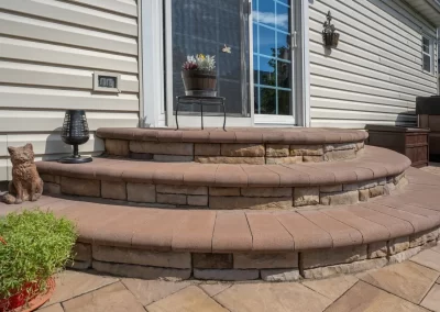 Three curved stone steps, part of expert hardscaping by Solid Brick Contracting MD, lead to a patio door accented with potted plants and a decorative cat statue.