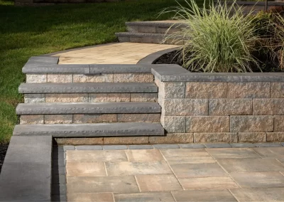 Stone steps and a retaining wall beside a landscaped grassy area in MD, featuring decorative paving and tall ornamental grass, showcase expert hardscaping and landscaping design.