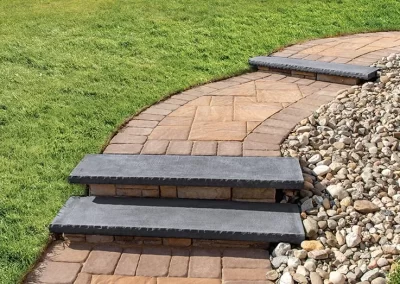 Curved stone pathway with steps, bordered by grass on one side and decorative rocks on the other—expertly crafted by Solid Brick Contracting to enhance your landscaping and hardscaping design.