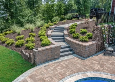 Curved stone steps with brick walls by Solid Brick Contracting lead up a landscaped garden hillside beside a patio, showcasing expert hardscaping in Aberdeen.