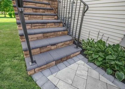 Stone steps with a black metal railing leading up to a house in Aberdeen, enhanced by lush landscaping and a paved walkway—crafted with care by Solid Brick Contracting.