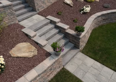 Stone steps and retaining walls by Solid Brick Contracting lead to a beautifully landscaped yard in MD, accented with potted flowers, lush grass, and vibrant flower beds.