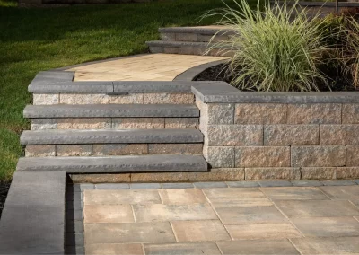 Stone steps and a retaining wall by Solid Brick Contracting enhance this Aberdeen patio, featuring expert hardscaping and ornamental grass alongside the paved walkway.