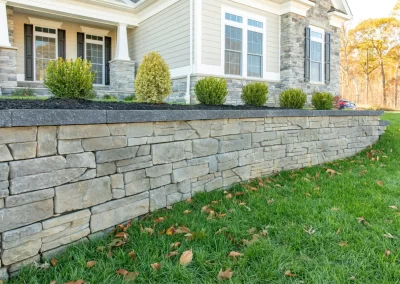 Stone retaining wall showcases expert hardscaping and landscaping in front of an Aberdeen home, bordered by green grass and scattered fallen leaves.