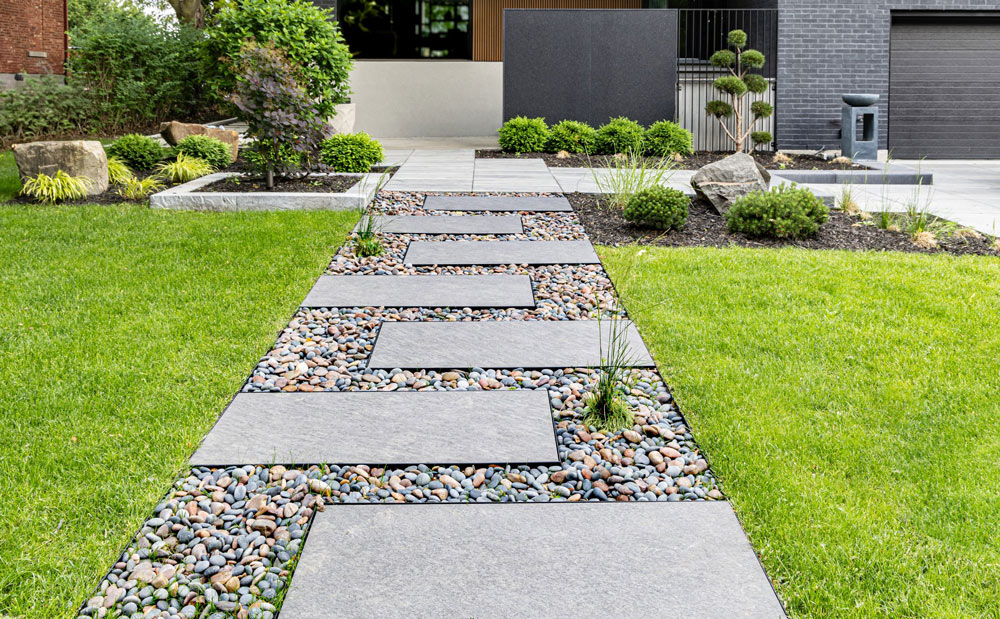 Large stone pavers set in gravel create a modern pathway through a landscaped green lawn and garden.